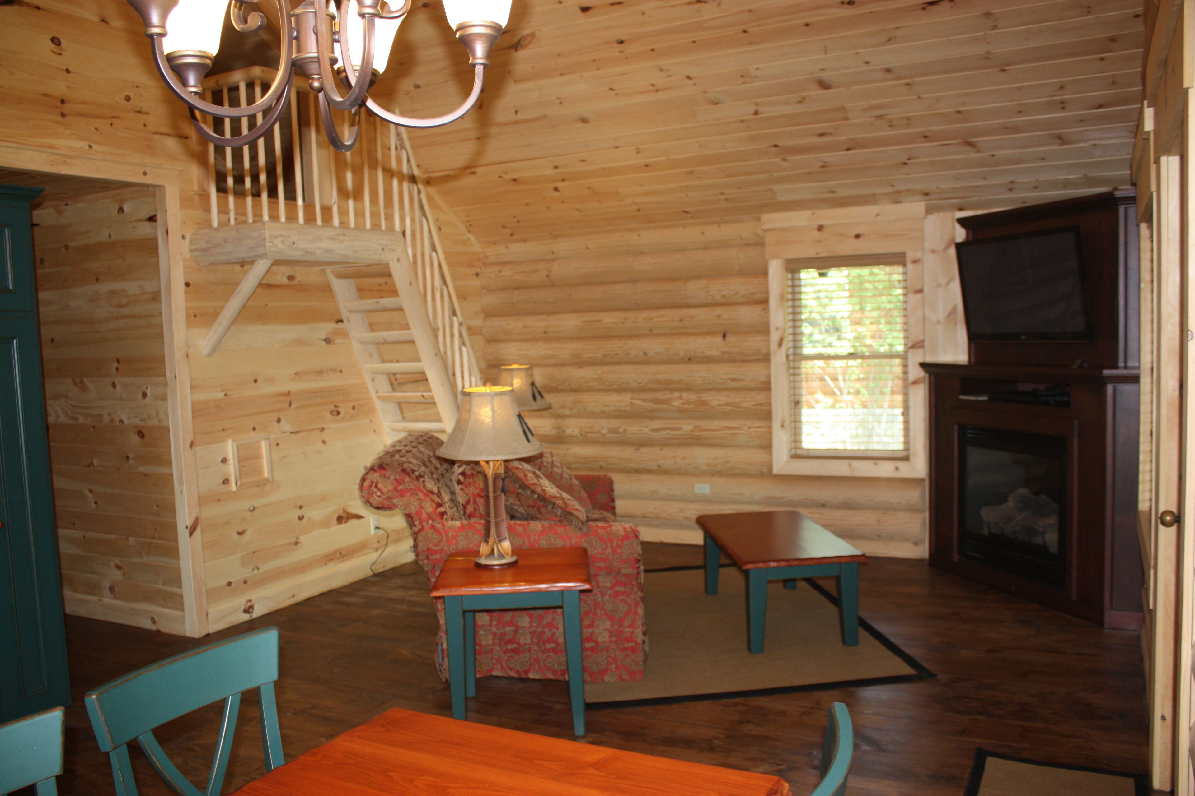 L’intérieur d’une cabane en rondins, avec un escalier, un canapé, une table et une cheminée.