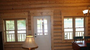 A log cabin interior with a wooden door, two windows with blinds, a table with chairs, and a lamp. - Lake Parlin Lodge & Cabins (Jackman)