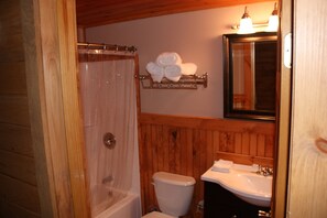 A bathroom with a wooden interior, a white toilet, a sink with a mirror above it, and a towel rack with folded towels. - Lake Parlin Lodge & Cabins (Jackman)