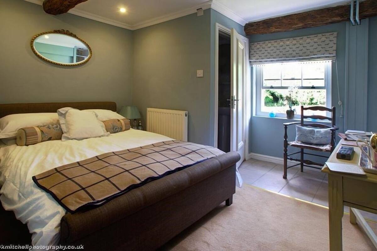 A bedroom with a large bed, a bedside table, a chair, a window with a view, and a mirror on the wall.