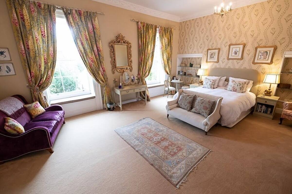 A bedroom with a large bed, two sofas, a dresser, and a mirror.