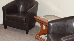 A room with a dark brown leather armchair and a wooden side table with a glass top. - The Northdale Hotel Ltd (Skegness)
