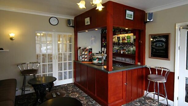 A bar area with a wooden counter, stools, and a clock on the wall. - The Northdale Hotel Ltd (Skegness)