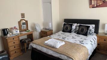 A neatly arranged bedroom with a bed, bedside tables, a desk, a chair, a mirror, and a wall-mounted artwork.