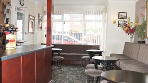 A bar area with a wooden counter, a sofa, and two round tables with stools. - The Northdale Hotel Ltd (Skegness)