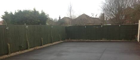 A paved outdoor area with a green fence, a metal railing, and a building in the background.