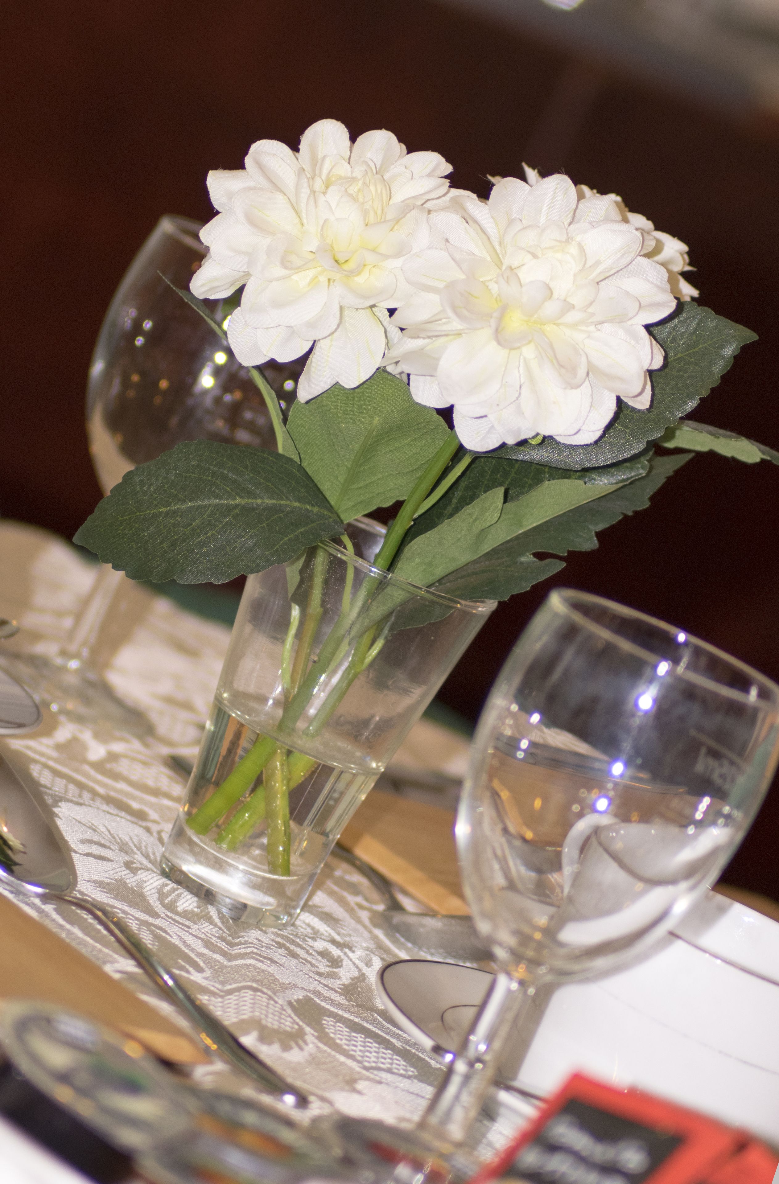 A table with a vase containing white flowers and two clear glasses.