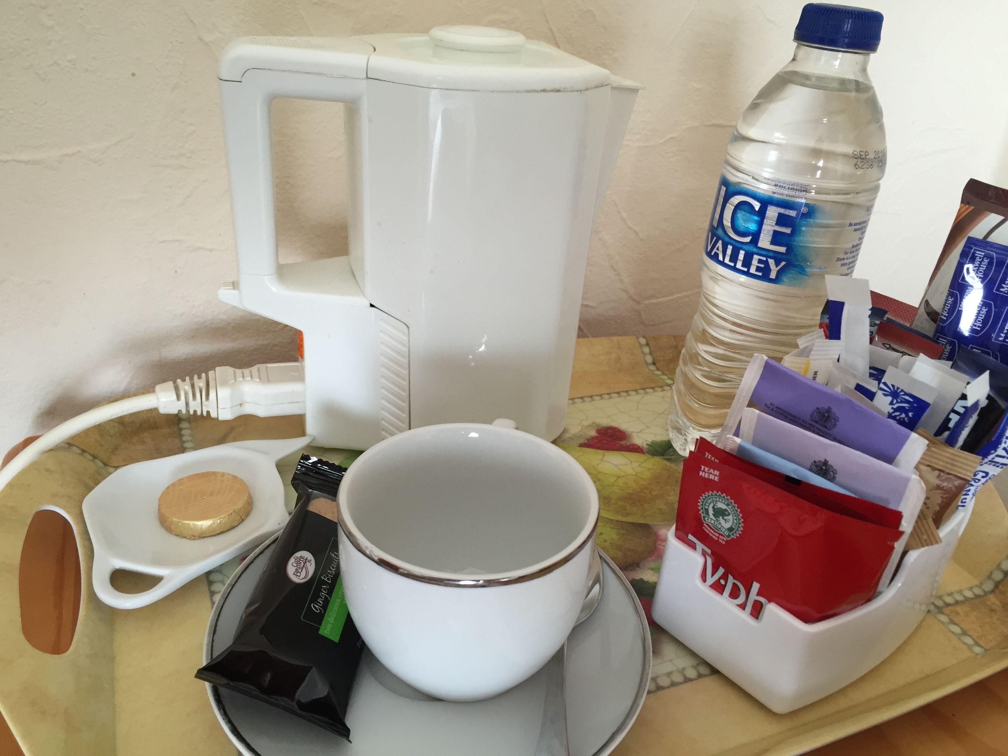 A tray with a coffee maker, a cup, a bottle of water, a tea bag, and a small container with a lid.