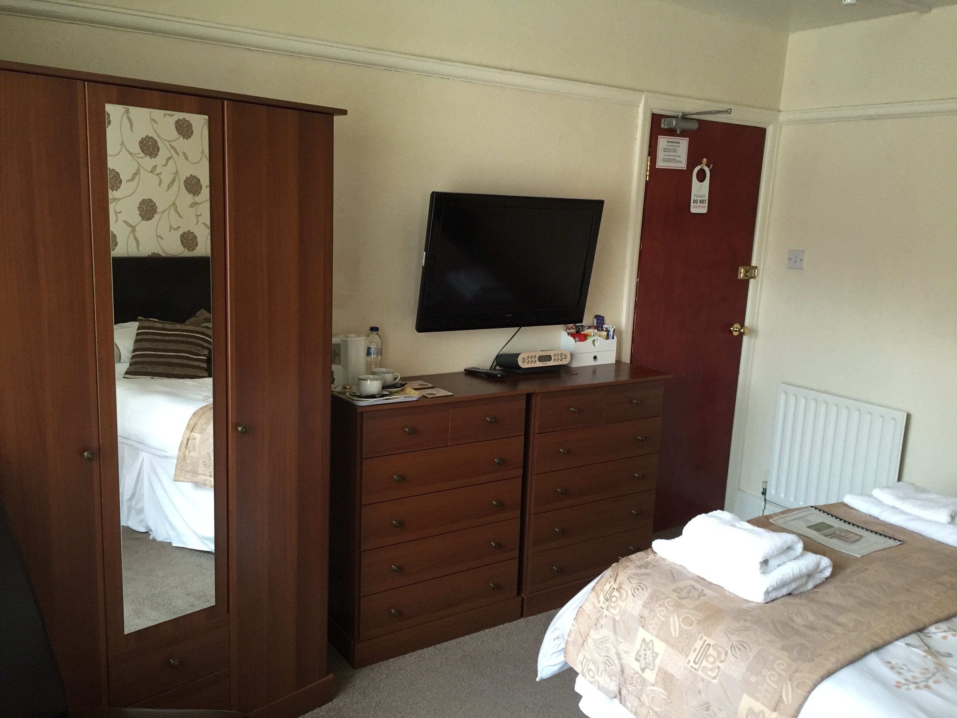 A hotel room with a bed, a dresser, a television, and a door with a 'Do Not Disturb' sign.