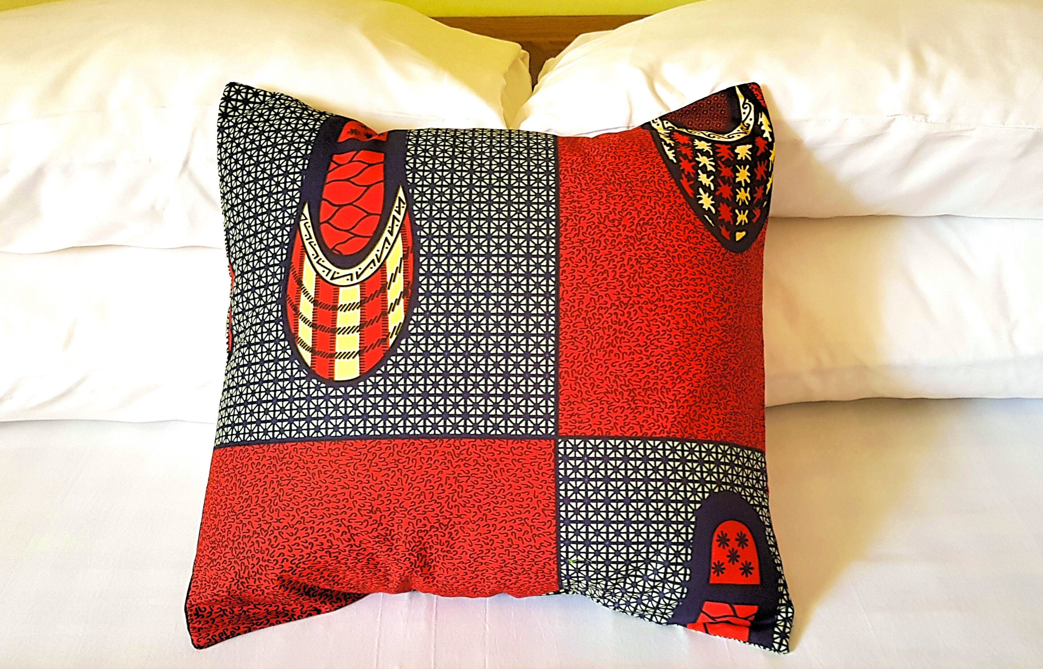 A bed with white sheets and a pillow featuring a geometric pattern with red, black, and yellow accents.