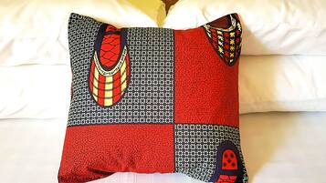 A bed with white sheets and a pillow featuring a geometric pattern with red, black, and yellow accents.