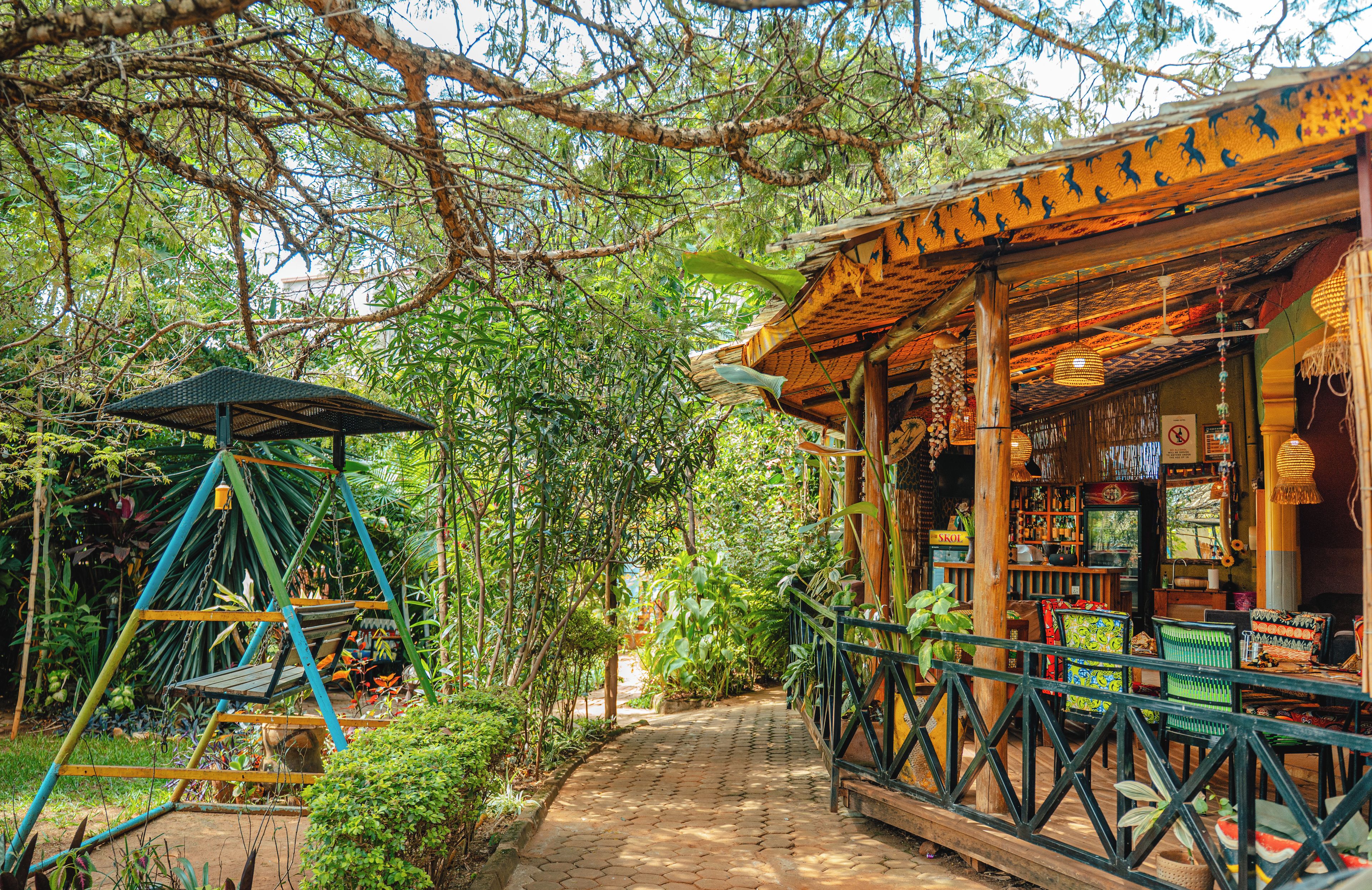 A rustic wooden structure with a thatched roof, surrounded by lush greenery and a paved pathway.