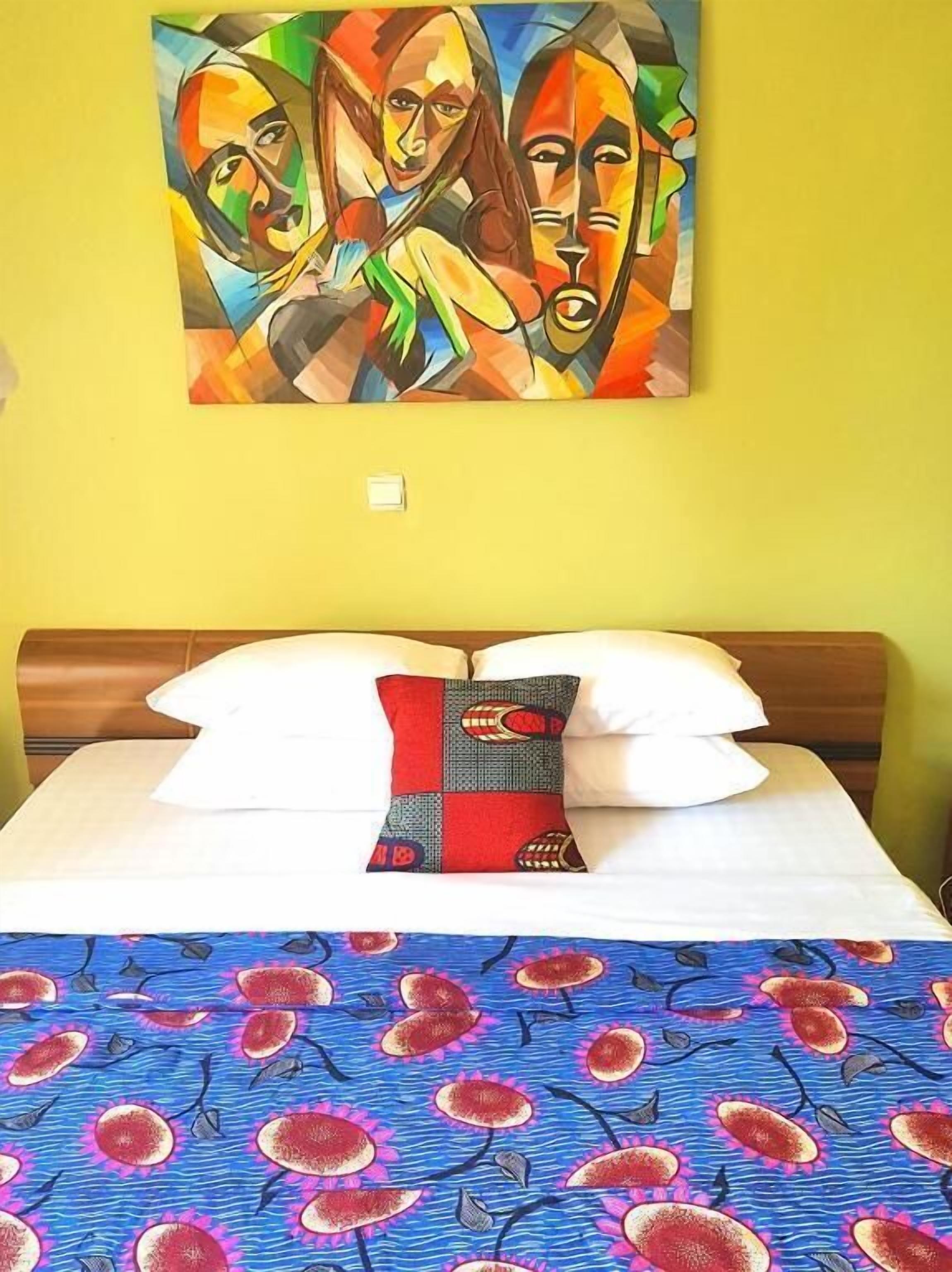 Une chambre d’hôtel avec un lit, un tableau coloré accroché au mur et une couvre-lit à motifs.