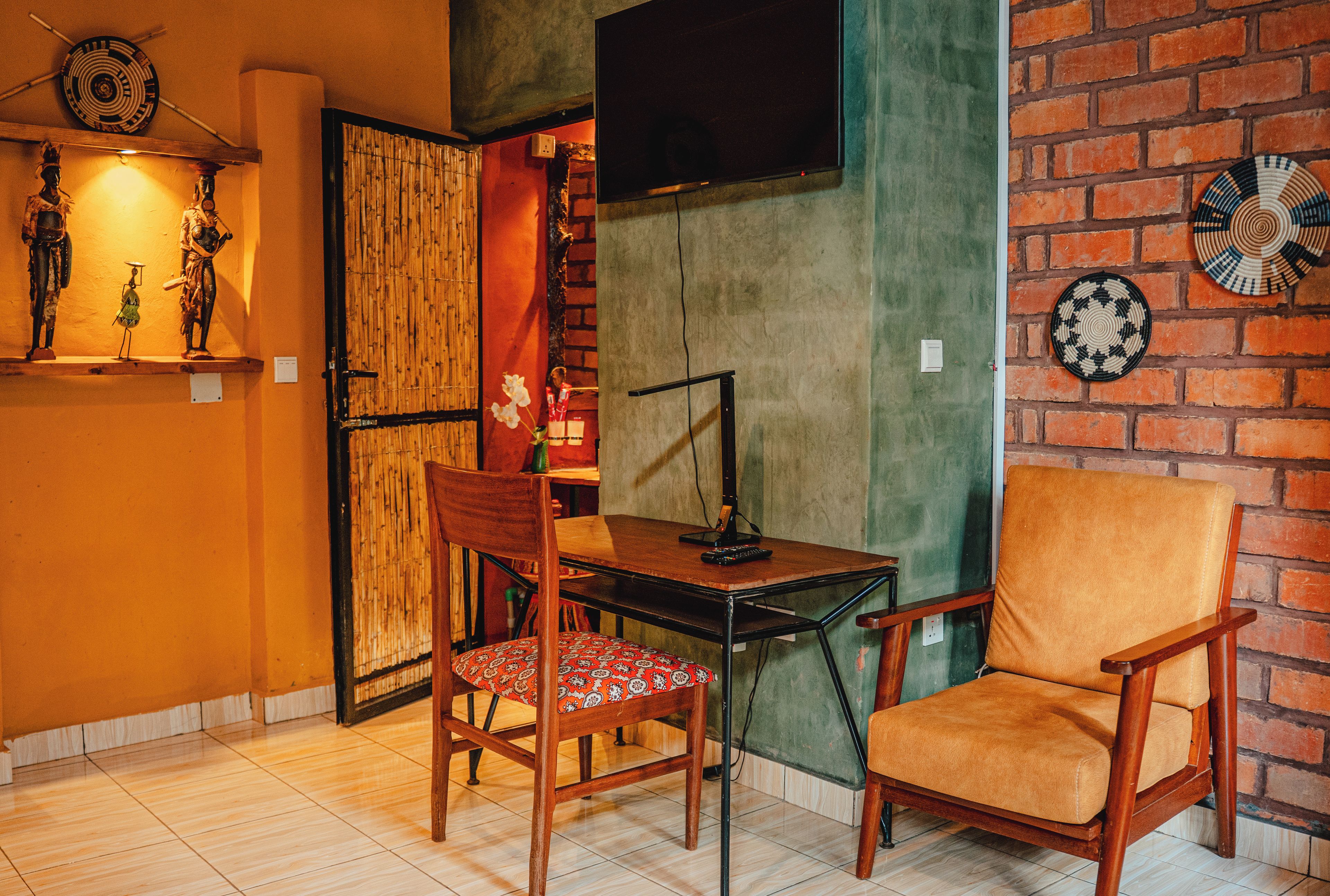 A room with a brick wall, a television mounted on it, a table with a chair, and a shelf with decorative items.