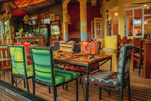 A dining area with a wooden table, chairs with patterned upholstery, and a view of the street outside. - Yambi Guesthouse (Kigali)