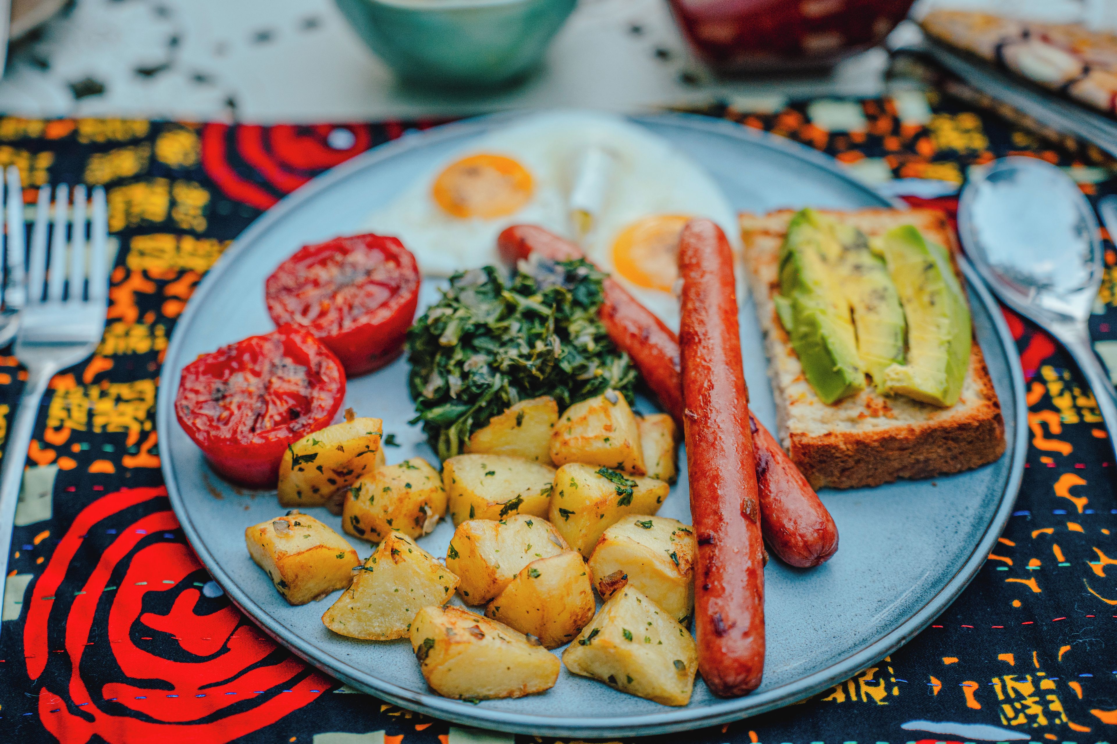 A plate with food items including potatoes, sausages, and avocado on toast.