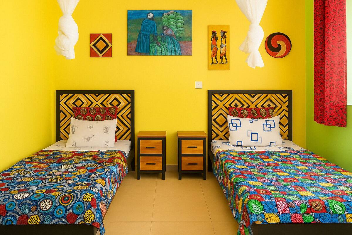 A room with two beds, each with a patterned bedspread, a painting on the wall, and a nightstand between the beds.