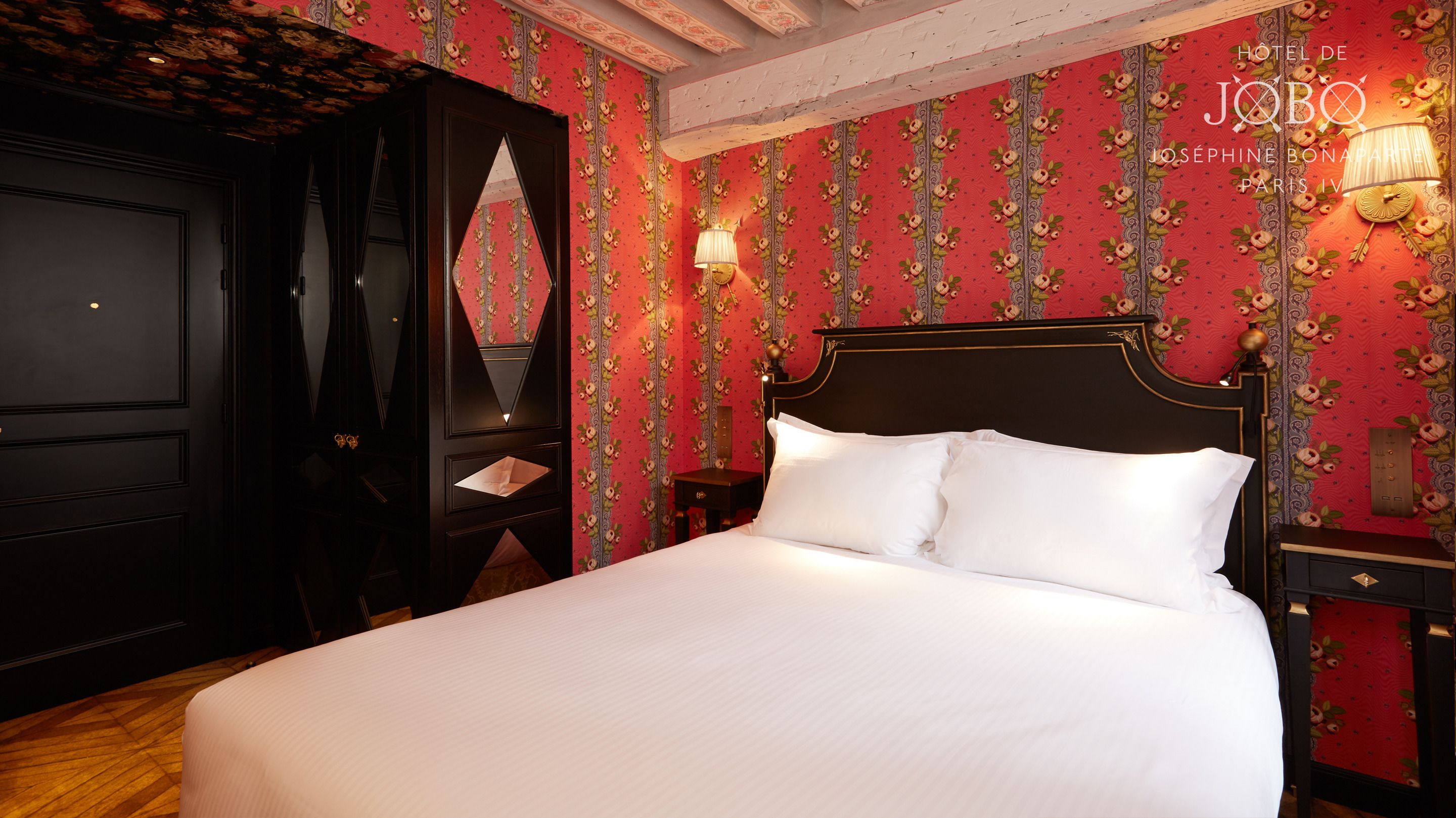Ein Hotelzimmer mit einem großen Bett, einer dunkelholzigen Tür und blumigem Wandpapier.