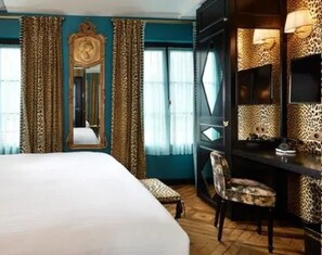 A hotel room with a large bed, a desk with a chair, a mirror, and leopard print decor. - Hôtel de JoBo (Paris)