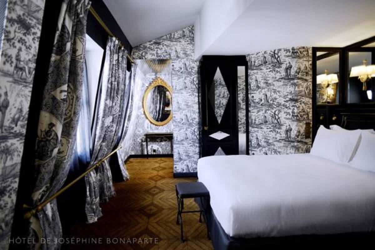 A hotel room with a large bed, a mirror, and a nightstand.