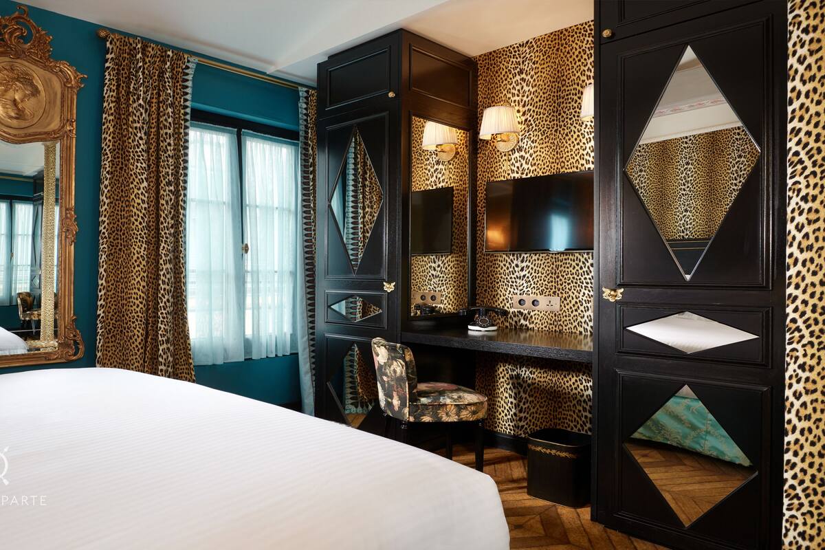 A hotel room with a large bed, a desk with a chair, a vanity with a mirror, and leopard print decor.
