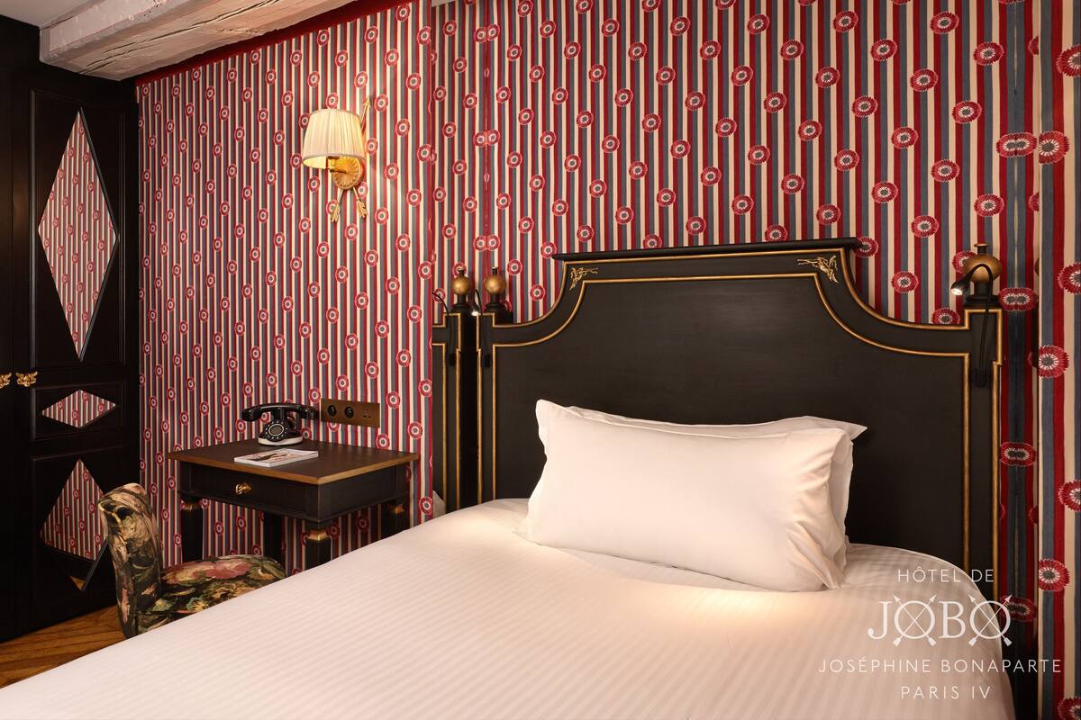A hotel room with a large bed, a desk with a telephone, and a mirror on the wall.