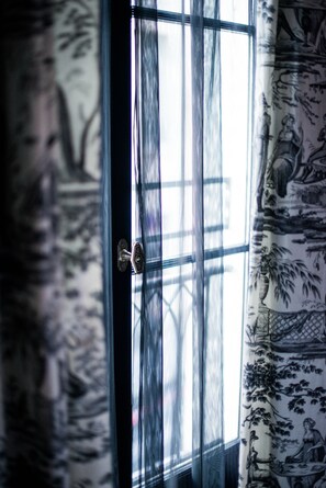 A window with a view of a building outside, a door with a handle, and patterned curtains. - Hôtel de JoBo (Paris)