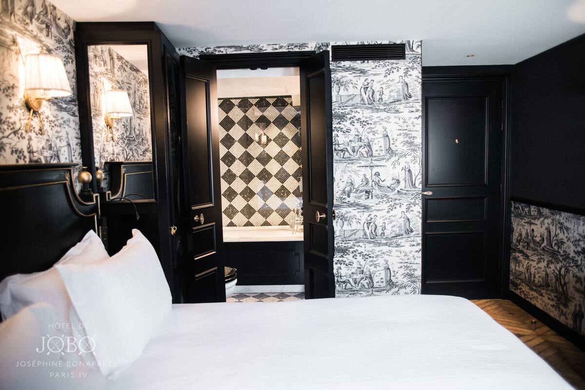 A hotel room with a bed, a wardrobe, a mirror, and a bathroom visible through an open door.