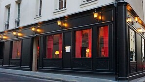 A corner building with black-framed windows and warm interior lighting. - Hôtel de JoBo (Paris)