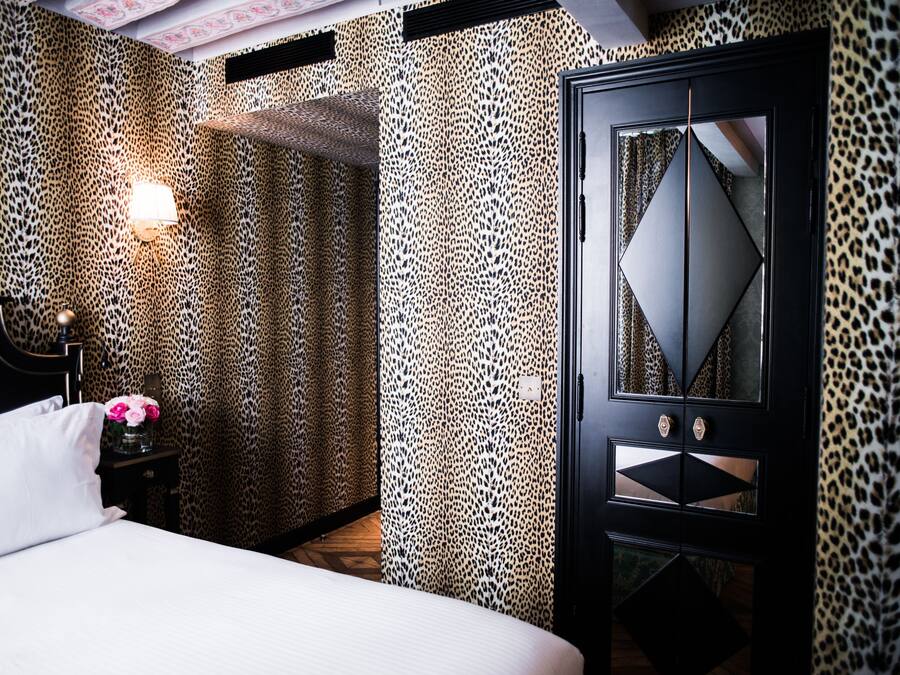 Een slaapkamer met een bed, een nachtkastje met een bloevas en een garderobe met een spiegel.