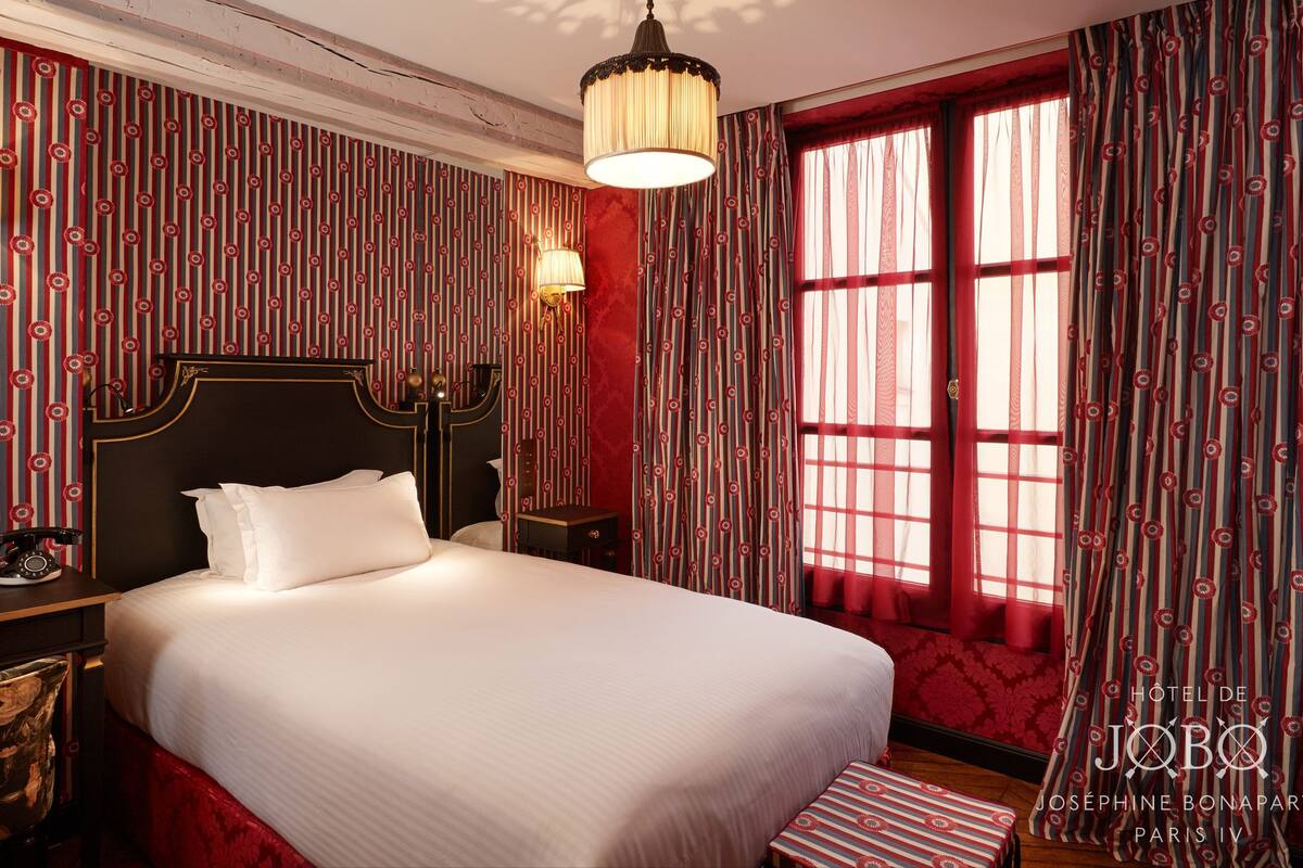 A hotel room with a large bed, a nightstand, a telephone, and a window with curtains.