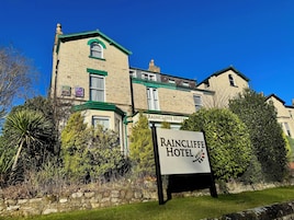 A traditional brick building with a green roof and a sign for Raincliffe Hotel.