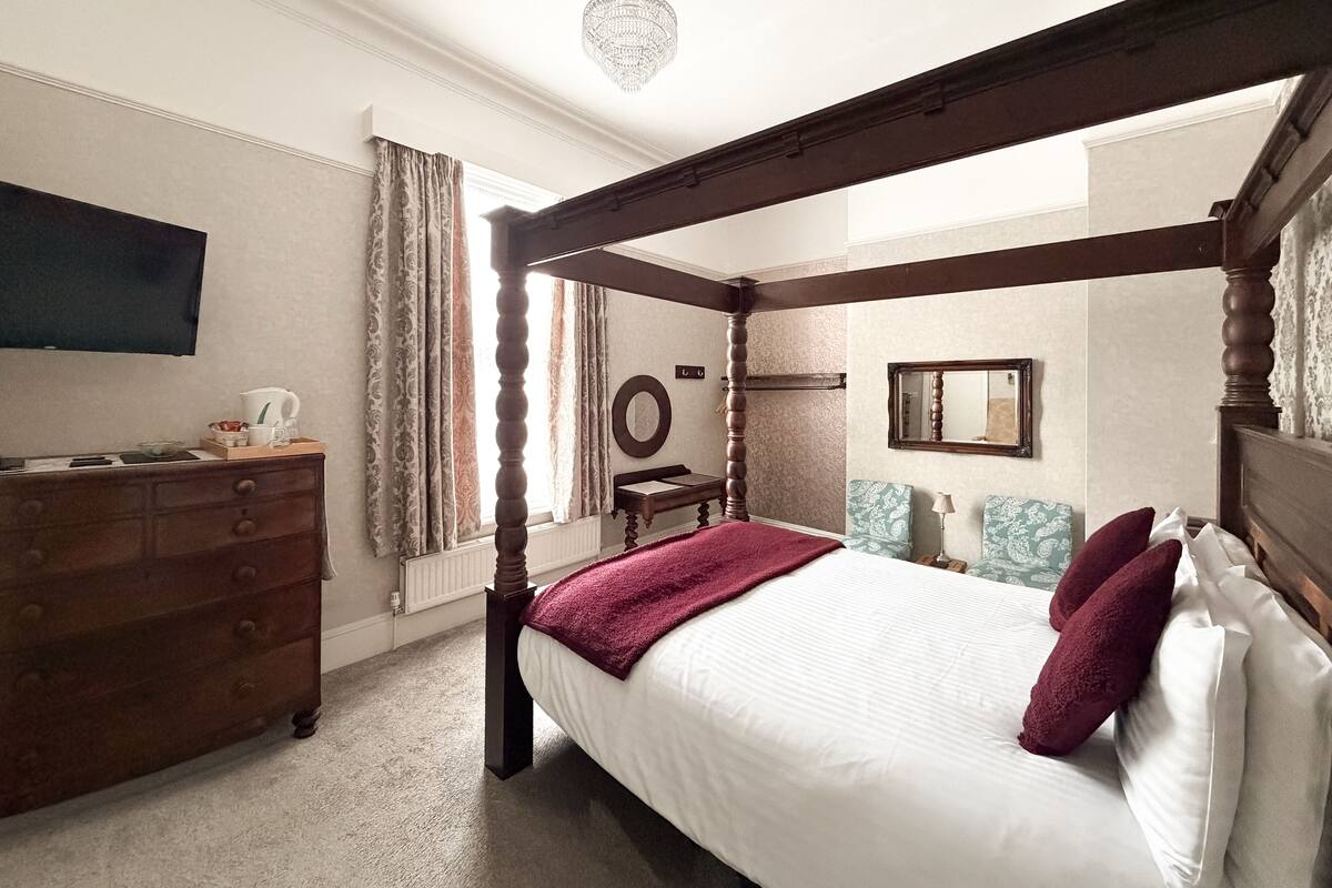 A four-poster bed with a wooden frame, a dresser with drawers, a mirror, and a chandelier.