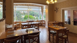 A dining area with wooden tables and chairs, large windows with curtains, and a chandelier. - Raincliffe Hotel (Scarborough)