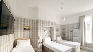 A hotel room with two single beds, a television, a wardrobe, and a window with curtains. - Raincliffe Hotel (Scarborough)