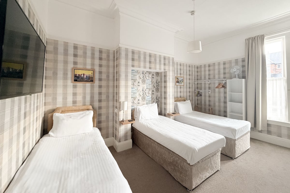 A hotel room with two single beds, a television, a wardrobe, and a window with curtains.
