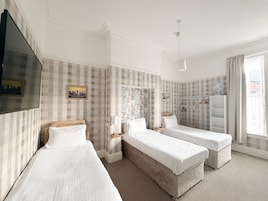 A hotel room with two single beds, a television, a wardrobe, and a window with curtains.