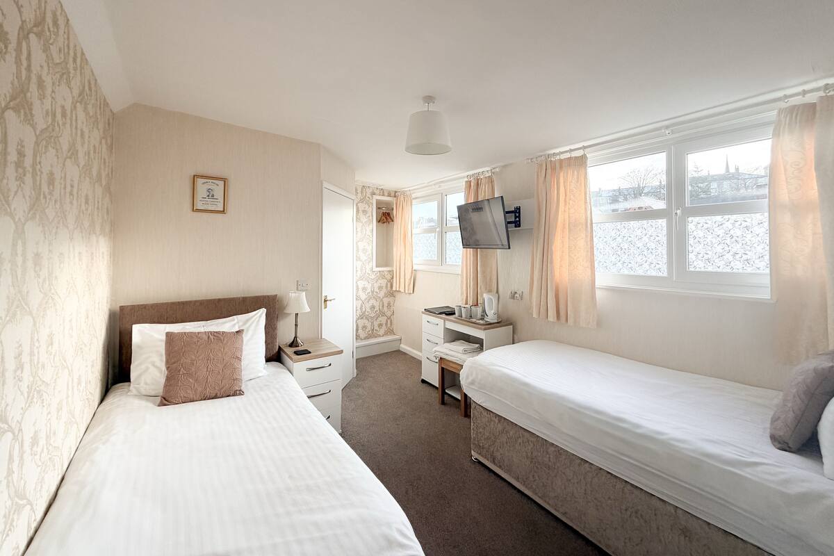 A hotel room with two beds, a TV, a desk, and a window with a view.