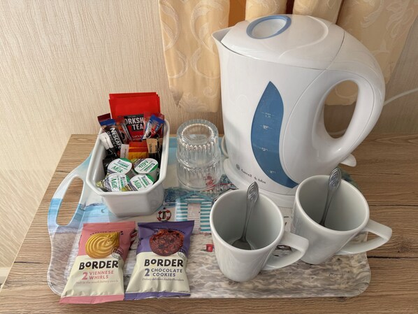 A table with a coffee maker, two mugs, a glass, a milk carton, and packets of cookies.