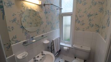 A bathroom with a sink, mirror, toilet, and a window.
