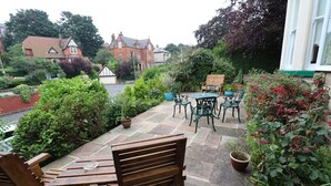 A patio with wooden furniture, potted plants, and a view of a red brick building in the background. - Raincliffe Hotel (Scarborough)