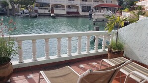 A balcony with a view of a canal, a boat, and a building with a white facade. - Villa 410D at Jolly Harbour (Jolly Harbour)