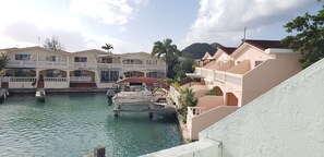 Un hotel frente al agua con varios balcones, un muelle con un barco y una montaña al fondo.