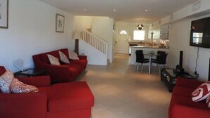 A spacious living area with a red sofa set, a dining table with chairs, and a kitchen in the background. - Villa 244D at Jolly Harbour (Jolly Harbour)