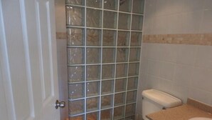 A bathroom with a glass shower enclosure, a toilet, and a sink. - Villa 244D at Jolly Harbour (Jolly Harbour)