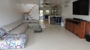 A modern living room with a sectional sofa, a wooden entertainment unit, and a large TV. - Villa 227E at Jolly Harbour-Adults Only (Jolly Harbour)