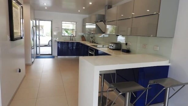 A modern kitchen with a central island, bar stools, and a view of the outside. - Villa 227E at Jolly Harbour-Adults Only (Jolly Harbour)