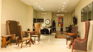 A spacious living area with a large armchair, a smaller chair, and a round table. There is a clock on the wall and a colorful abstract painting. - Ritz Hotel (Angeles City)