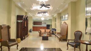 A spacious lobby with a high ceiling, a chandelier, a ceiling fan, and a reception desk in the background. - Ritz Hotel (Angeles City)
