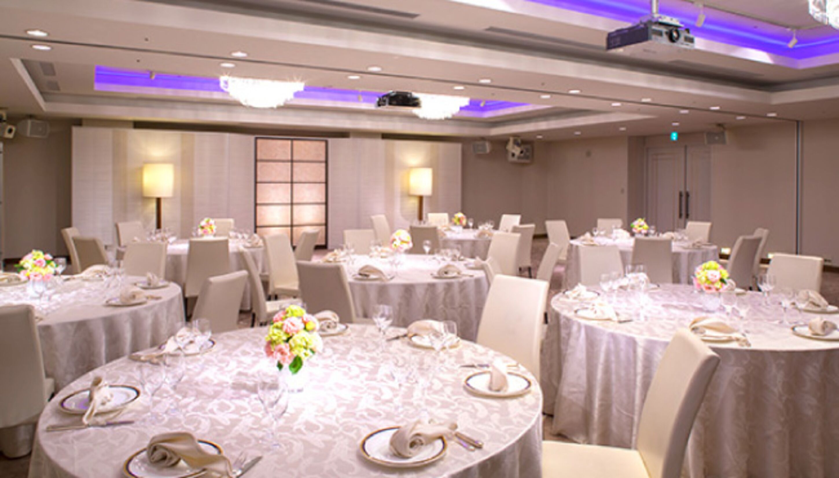 A conference room with round tables, each set with plates, cutlery, and floral centerpieces.